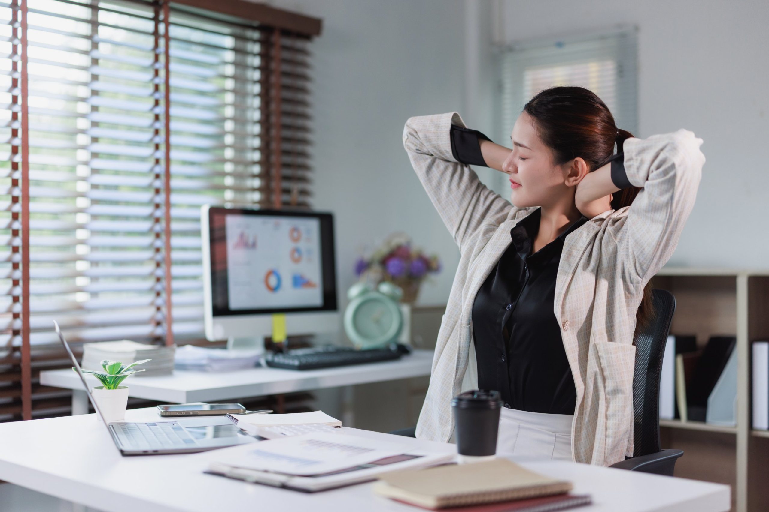 Woman stretching her neck and shoulders at her office desk after a long day of work